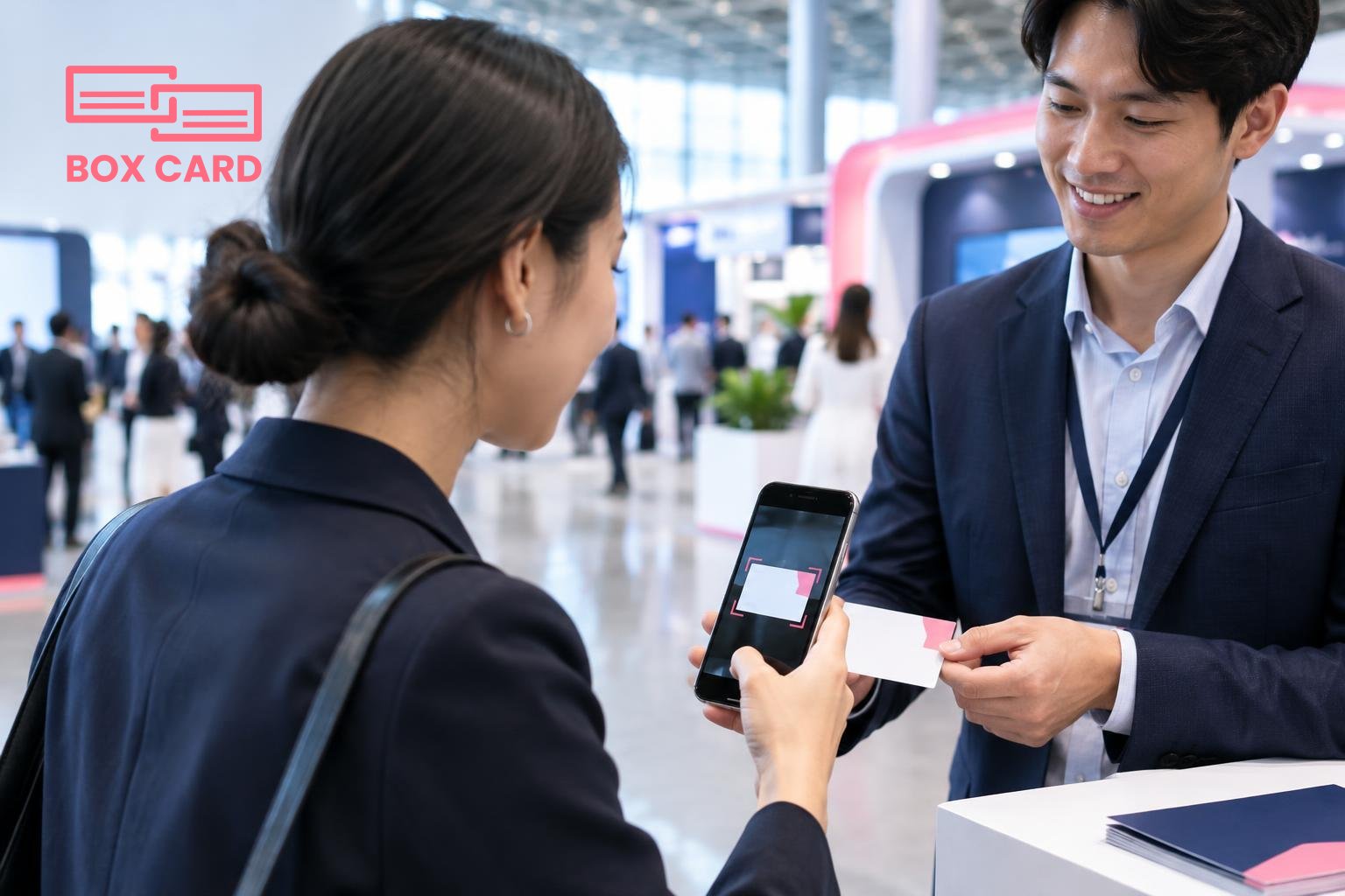 싱가포르 전시장 로비에서 참가자가 스마트폰으로 명함을 스캔하고 Boxcard 앱의 스캔 확인 화면이 보이는 실사 사진