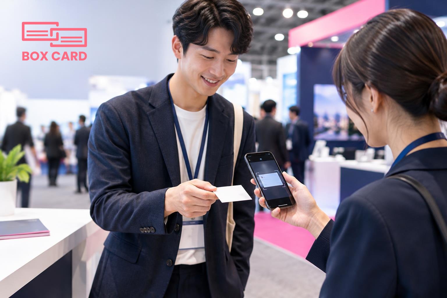 전시회 부스 앞에서 명함을 건네는 두 참석자, 한 손에는 스마트폰으로 Boxcard 앱을 열어 명함을 스캔하는 장면, 편집된 사진 스타일